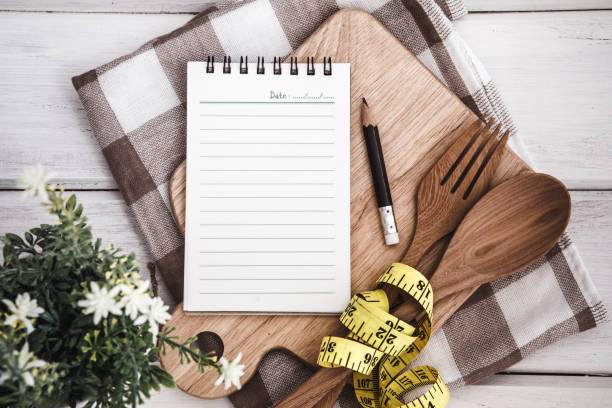 istock Line Notepad on chopping board with wooden fork and spoon and the measuring tape on white table , recipes food or diet plan for healthy habits shot note background concept 857241480