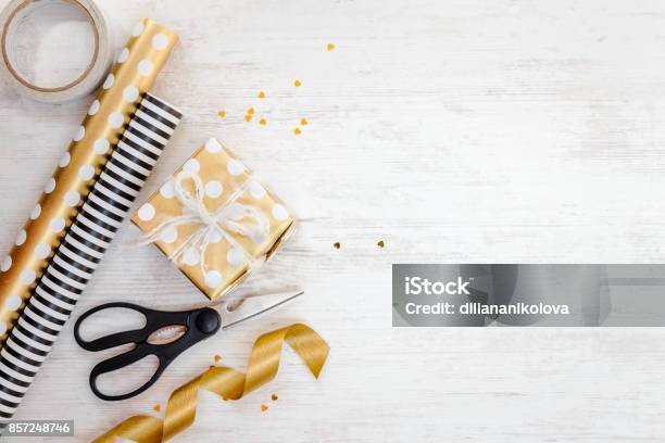 Gift Box Wrapped In Golden Dotted Paper And Wrapping Materials On A White Wood Old Background Empty Space Stock Photo - Download Image Now
