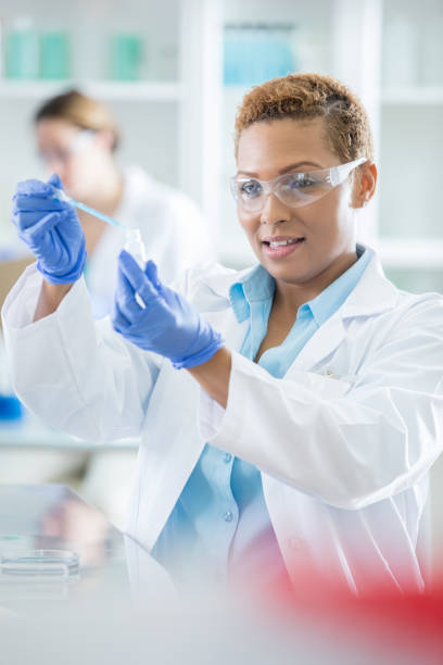 istock Mid adult female lab technician introduces solution to small bottle 857271972