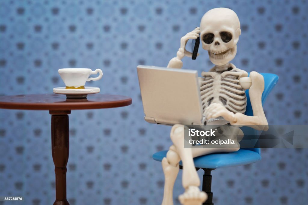 Skeleton working day Skeleton talking with smartphone while working with laptop Dead Stock Photo