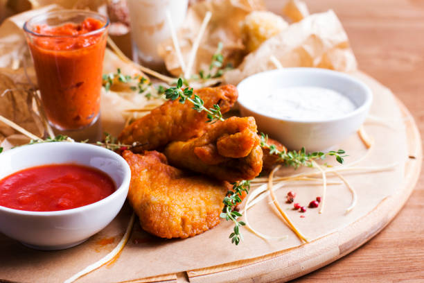 alas de pollo picantes al horno con aperitivos y salsas en una tabla de madera redonda - wing spicy chicken wings chicken sauces fotografías e imágenes de stock