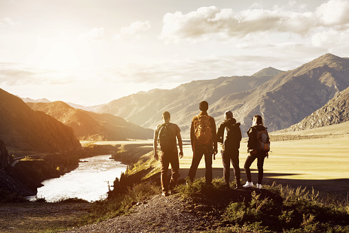 Group of four people stands on mountains and river backdrop. Travel expedition trekking concept with space for text