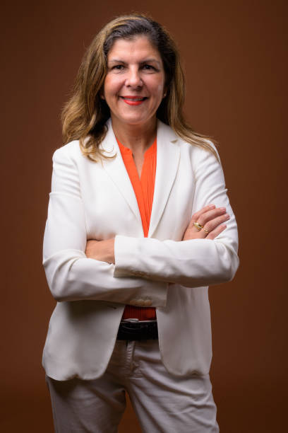 studio shot of mature businesswoman wearing pant suit against colored background - fato de senhora imagens e fotografias de stock