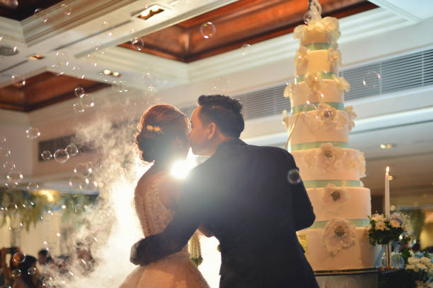 Groom kisses bride in front of cake in wedding ceremony in hall Groom kisses bride in front of cake in wedding ceremony in hall asian wedding stock pictures, royalty-free photos & images