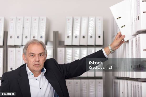 Older Man With White Shirt Puts A Documents Folder On A Shelf Stock Photo - Download Image Now