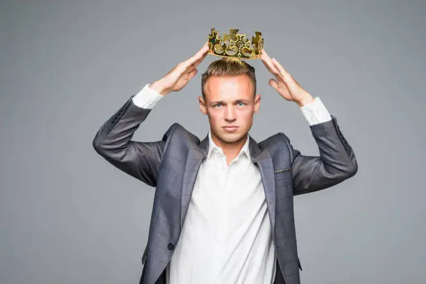 Photo of Business king. Confident businessman in crown standing isolated on gray