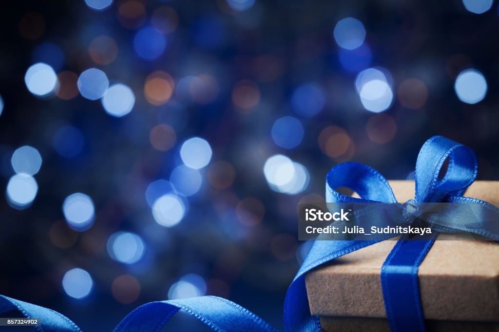 Christmas gift box or present with bow ribbon on magic blue bokeh background. Christmas gift box or present with bow ribbon on magic blue bokeh background. Copy space for greeting text. Blue Stock Photo