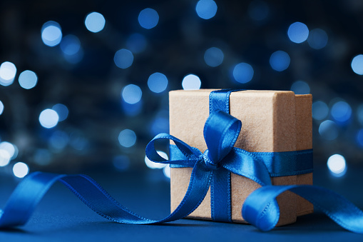 Holiday gift box or present with bow ribbon against blue bokeh background. Magic christmas greeting card. Copy space for data or design.