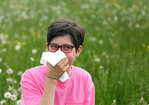 Allergic Child with glasses blows his nose in the middle of the meadow with dandelion