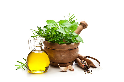 Front view of a wooden mortar filled with fresh herbs shot on white background, an olive oil bottle, two garlic cloves and two wooden serving scoops with salt and peppercorns complete the composition. DSRL studio photo taken with Canon EOS 5D Mk II and Canon EF 100mm f/2.8L Macro IS USM