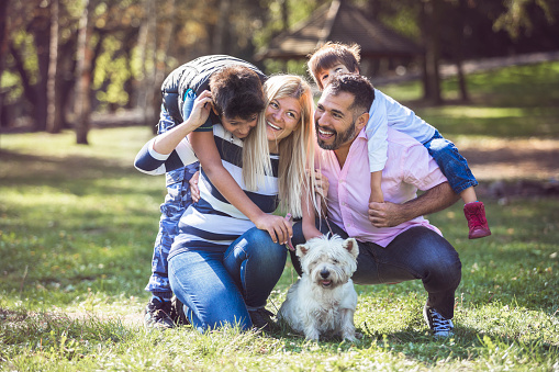 Mixed-race family enjoying in public park with cute white dog