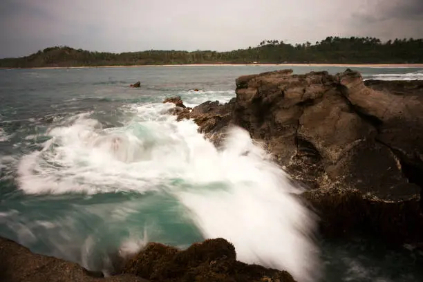 Blue ocean waves crashing and splashing against brown rocks on the coast.