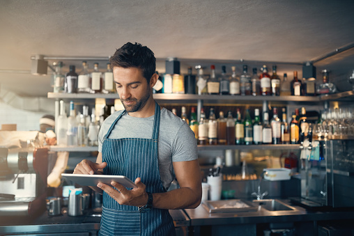 Shot of a young man using a digital tablet while working behind a bar counter