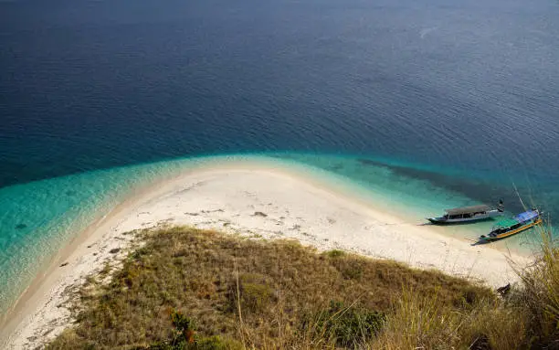 Top view of two boats at the coast of a white sand beach surrounded by  blue turquoise colored ocean water in Flores Indonesia.