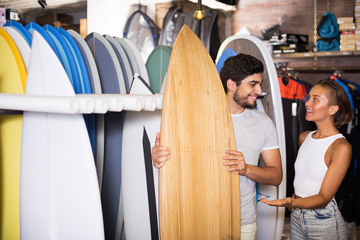 Adult man and woman choosing surfboards in the modern store