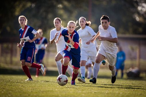 Teenage soccer player making an effort while running with soccer ball during a match against her opponents.