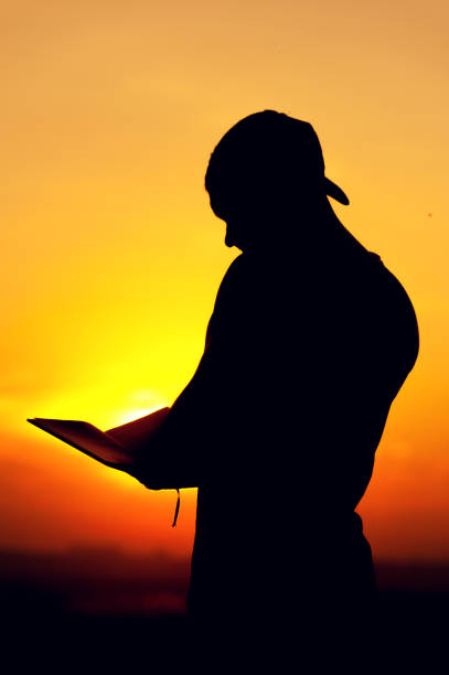 istock Silhouette of young man reading a book at sunset 857404400