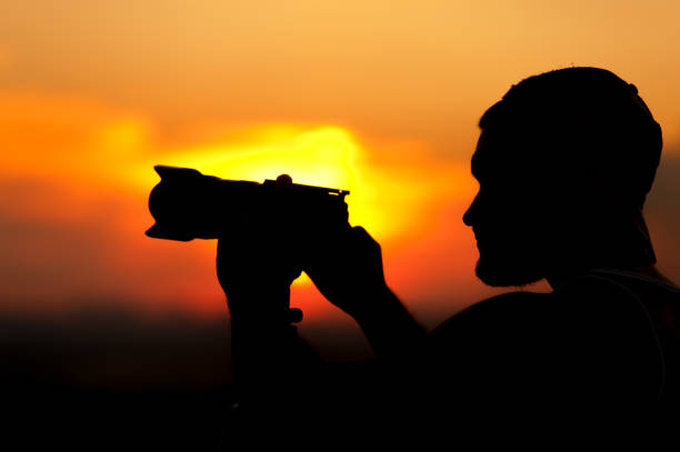 istock Silhouette of young man with camera at sunset time 857407172