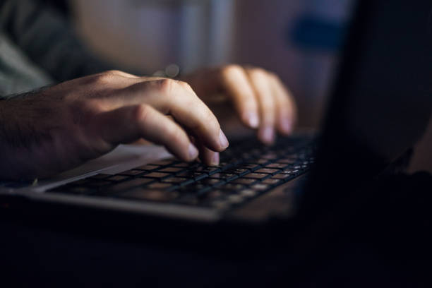 hombre sentado en el escritorio y trabajar en la computadora portátil en la noche - typing fotografías e imágenes de stock