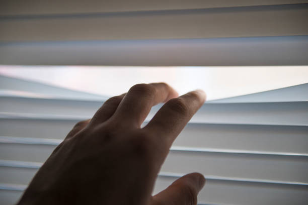 Close-up view of an unrecognizable person looking through shutter. Horizontal composition. Image taken with Nikon D800 and developed from Raw format. Unrecognizable person opening shutter to look around.