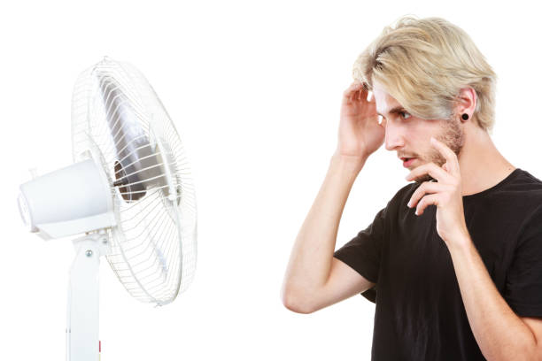 istock Young man fighting with wind from cooling fan 857449096