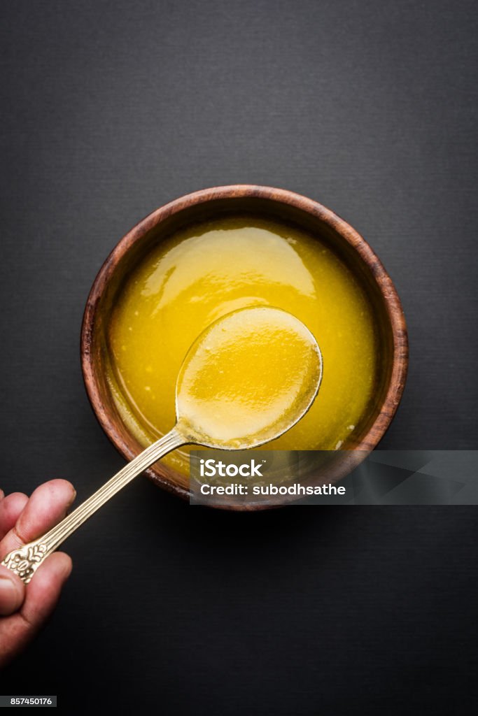 Ghee or clarified butter close up in wooden bowl and silver spoon, selective focus Ghee Stock Photo