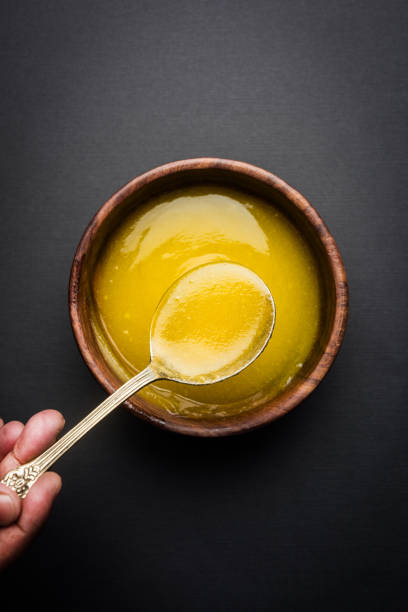 Ghee or clarified butter close up in wooden bowl and silver spoon, selective focus stock photo