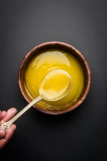 Photo of Ghee or clarified butter close up in wooden bowl and silver spoon, selective focus