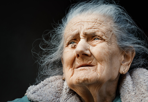 Portrait of a very old and tired of life wrinkled woman outdoors near the wall of her house