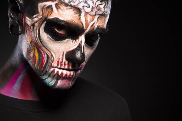 Close up portrait of man with colored skull make up. Face art, male with scary face isolated on black background.