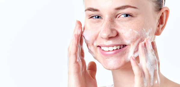 Teenager skincare. Smiling beautiful teen girl with freckles and blue eyes using foaming cleanser. Face washing concept isolated on white background.
