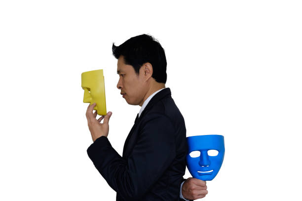 Businessman wearing yellow mask and hides blue mask in the hand behind his back on white background with clipping path.