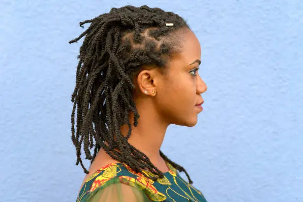 Side view head shot portrait of a pretty young African American woman with dreadlocks over a textured blue background