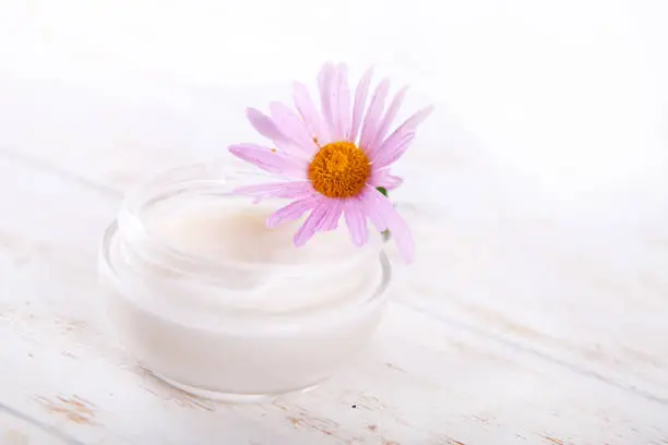 face-cream and flower on a white wooden background. natural organic cosmetic facial. space for text Close up