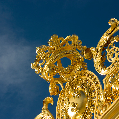 Paris, France - January 11, 2010: Fragment of golden entrance gates to the Versailles Palace (Chāteau de Versailles) on a sunny summer day. The Versailles is a Royal Palace in Versailles which is a suburb of Paris, some 20 kilometres southwest of the French capital.