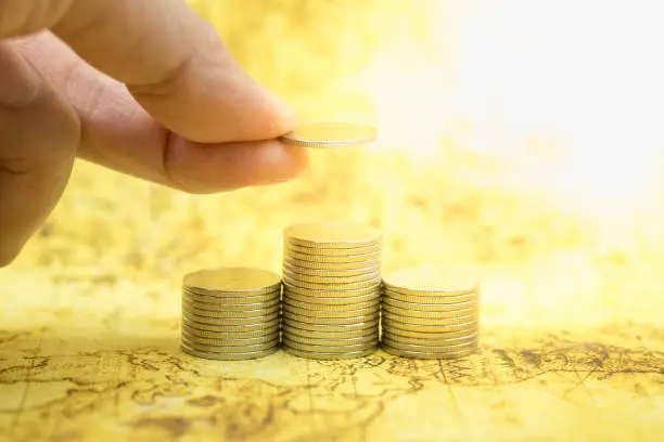 Photo of Money, business and Risk concept. Close up of unsteady stack of silver coins on world map and man hand holding and put a coin to top of stack.