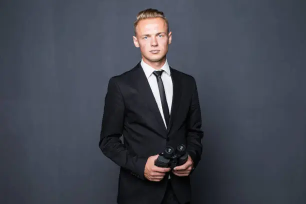 Photo of Businessman in suit looking through binoculars in hands with gray background