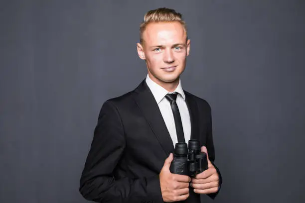 Photo of Businessman in suit looking through binoculars in hands with gray background