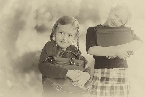 Adorable old-fashioned happy little 6 years old and 10 years old girls, back to school concept. Preschooler and schoolgirl sisters, schoolkids. Horizontal old vintage retro monochrome black and white photo.