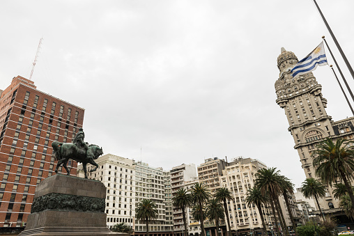 Montevideo, Uruguay - September 7, 2017: View of the statue of General Artigas along with  buildings, nature and the national flag at the square 'Plaza Independencia' in Montevideo, Uruguay