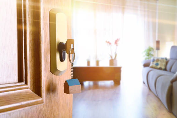 Open entrance door with furnished living room in the background Open entrance door detail of a house with keys in the lock and furnished living room in the background with golden light effect. property security stock pictures, royalty-free photos & images