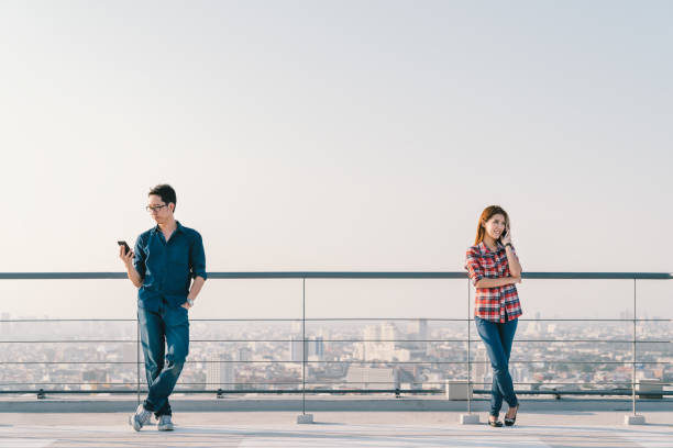 giovane coppia asiatica che usa telefonata e smartphone insieme sul tetto dell'edificio. dispositivo cellulare mobile o concetto di telecomunicazione informatica. sfondo vista paesaggio urbano, spazio di copia del cielo - roof men business city foto e immagini stock