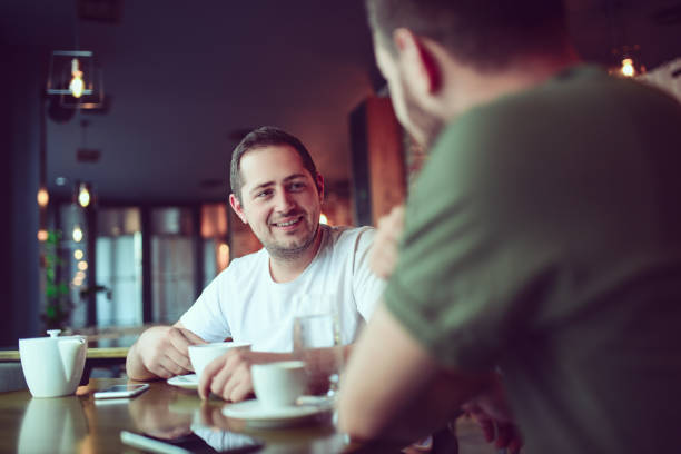 deux amis souriants boire du café et socialisation dans un cafe - friendship men two people male photos et images de collection