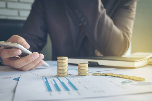 istock businessman using smart phone with stacked coins arranged at office desk and many document data graph in morning light, business concept. 857655648