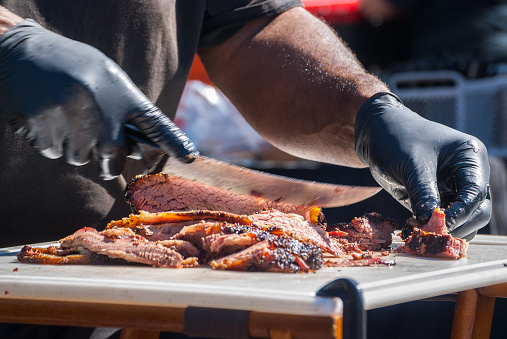 Steam raises as chef carves meat fresh out of the smoker at a summer fair.