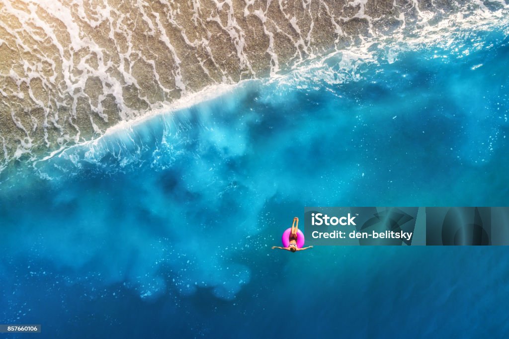 Vista aérea de joven mujer nadando en el anillo la rosa nadada en el mar transparente color turquesa en Oludeniz, Turquía. Paisaje de verano con chica, hermosas olas, agua azul al atardecer. Vista superior del abejón - Foto de stock de Playa libre de derechos