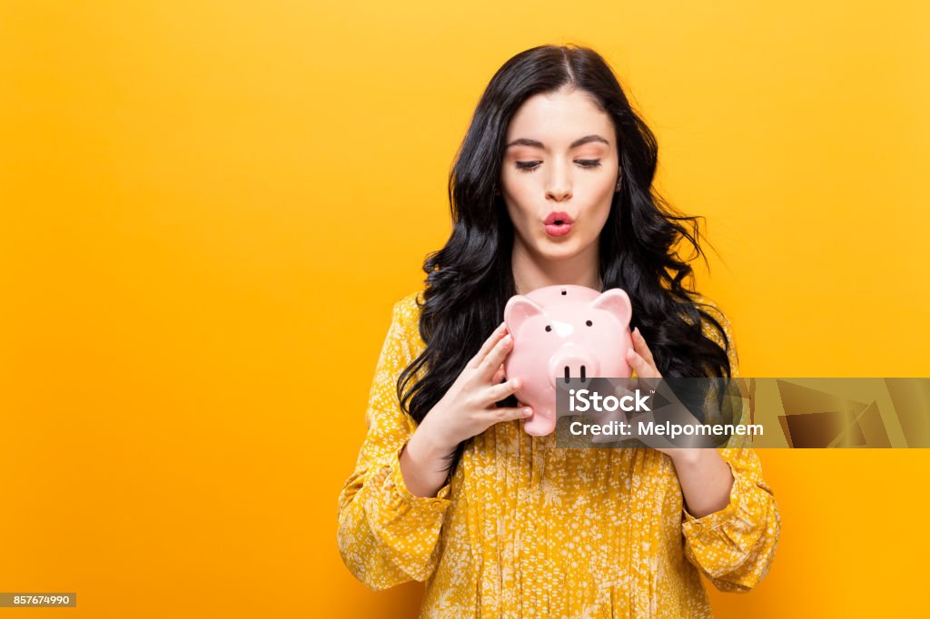 Young woman with a piggy bank Young woman with a piggy bank on a yellow background Savings Stock Photo