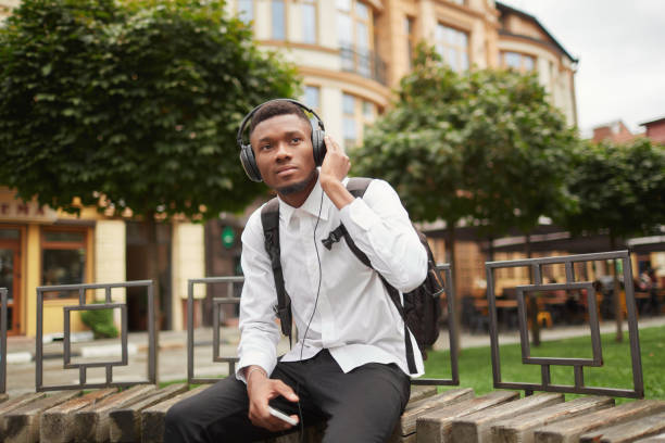 istock African student at break listening music at park 857700372