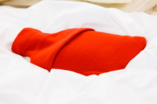 istock Warm red hot water bottle on white bedding 857705190