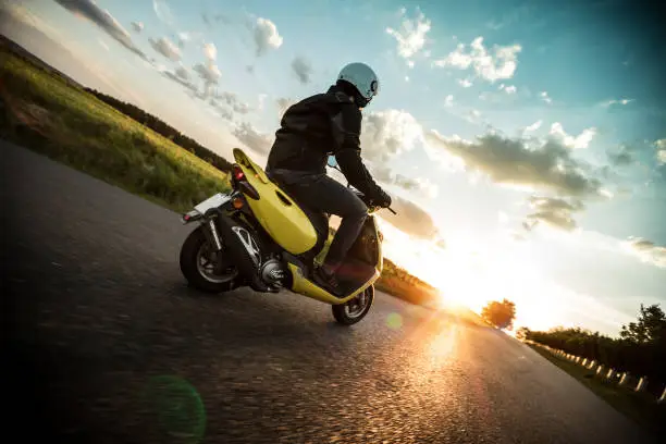 Man riding scooter on countryside during sunset.